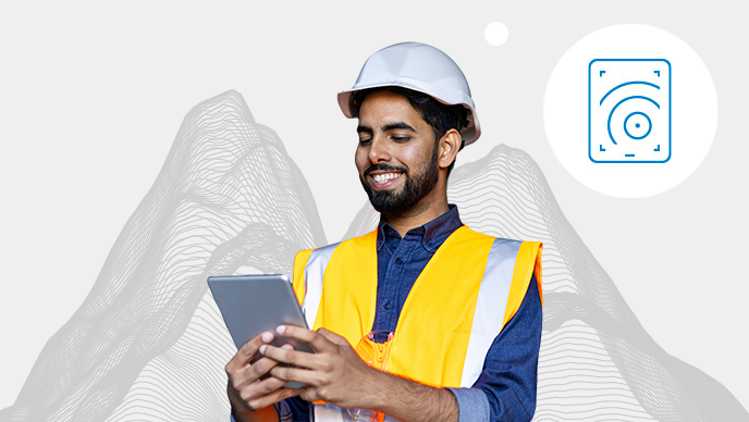 A man in an orange vest and white hard hat holding a tablet with an inset icon in a white circle