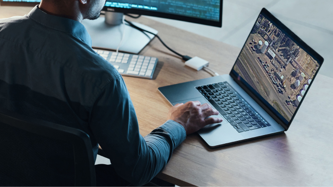A person using a laptop at a desk viewing a video of a facility and parking lot,A person using a laptop at a desk viewing a video of a facility and parking lot