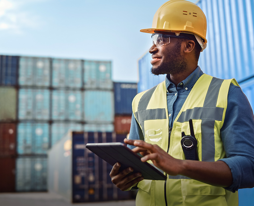 A digital animation of the Port of Rotterdam with traffic illuminated as it moves around the port, overlaid on a photo of a man next to a shipping container entering information onto a tablet