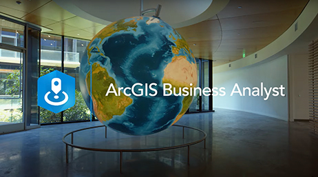 A modern office space with a large globe suspended in the center, overlaid with the ArcGIS Business Analyst name and logo in white