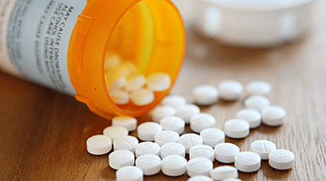 An orange pill bottle laying on its side with many little, round, white pills spill out onto a brown surface