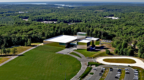 An aerial view of a large modern museum surrounded by a wide green field and an expanse of dense green trees