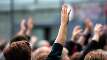 The tops of heads in a crowd of people, some of them with their hands raised