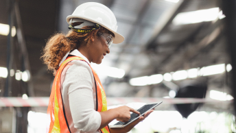 A person wearing a hard hat, safety glasses, and a safety vest using a tablet