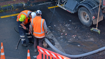 Two members of a construction crew wearing safety vests and hard hats working on a street segment
