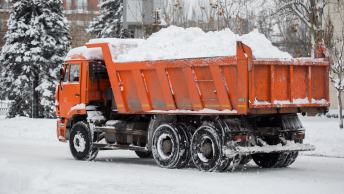 An orange, heavy duty truck hauling snow