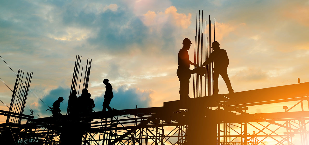 Construction workers on top of a building structure with a sunset in the background