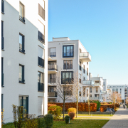 A row of modern white office buildings with tidy green lawns under a clear blue sunlit sky